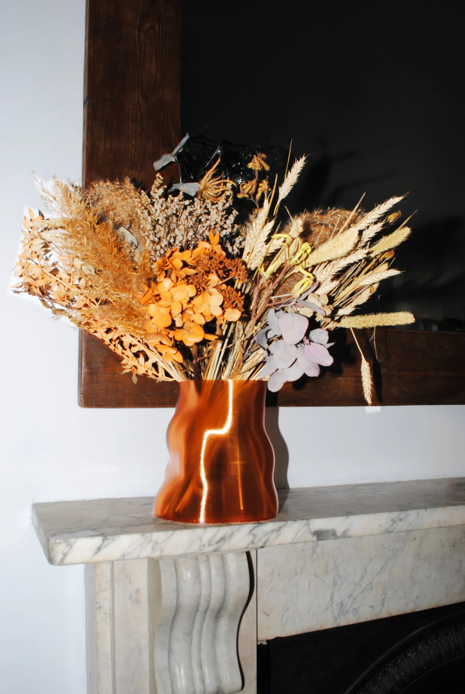 A Peski vase in Copper Orange filled with dried flowers on a marble mantelpiece