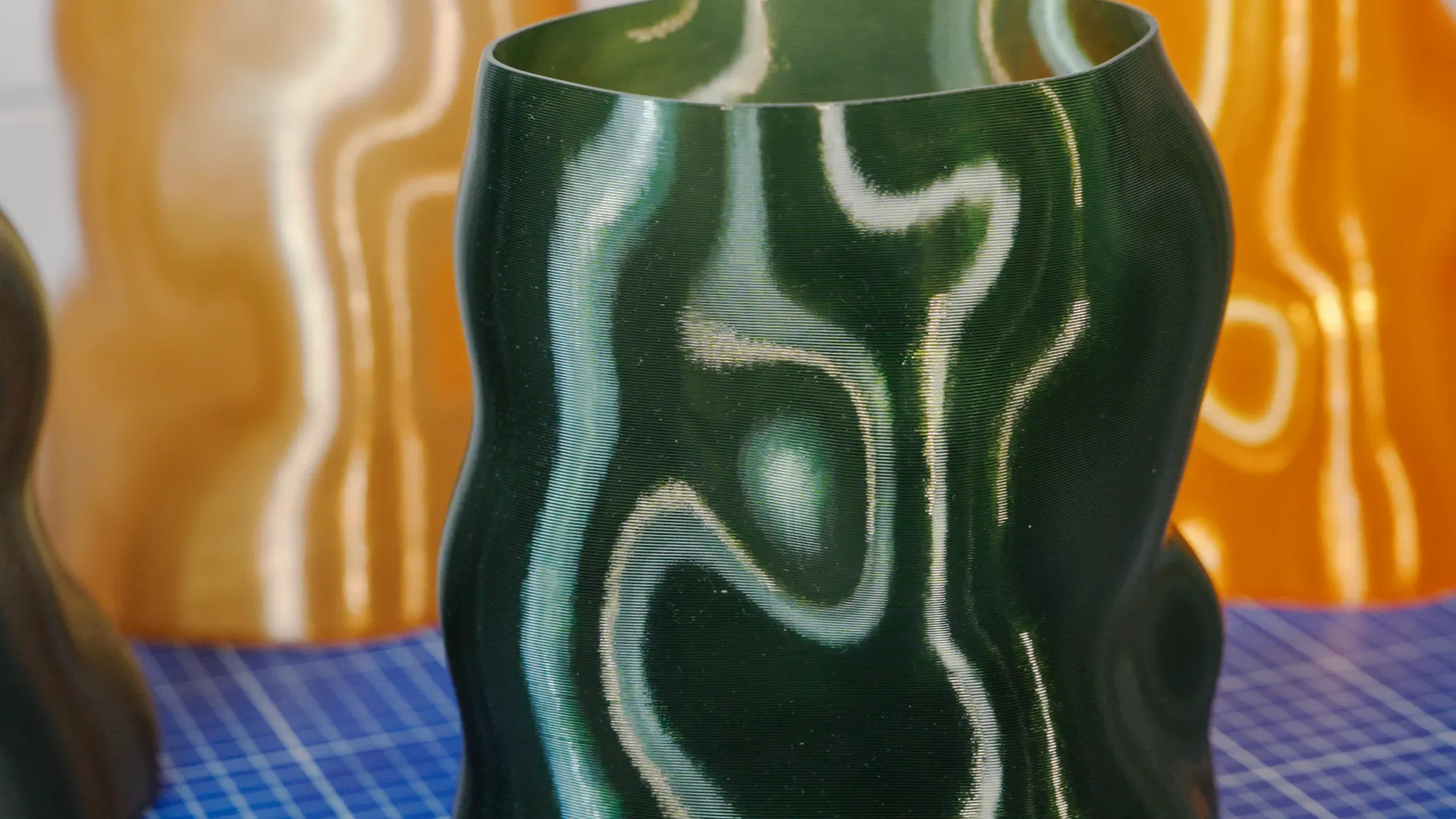 A Glass Green Peski vase on the workbench, with copper and orange vases behind