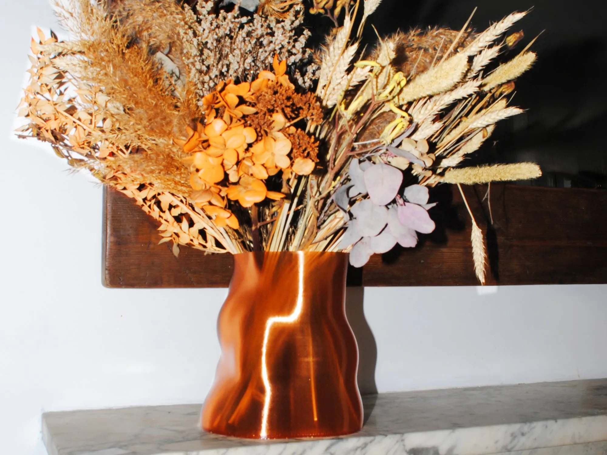 A Peski vase in Copper Orange filled with dried flowers on a marble mantelpiece
